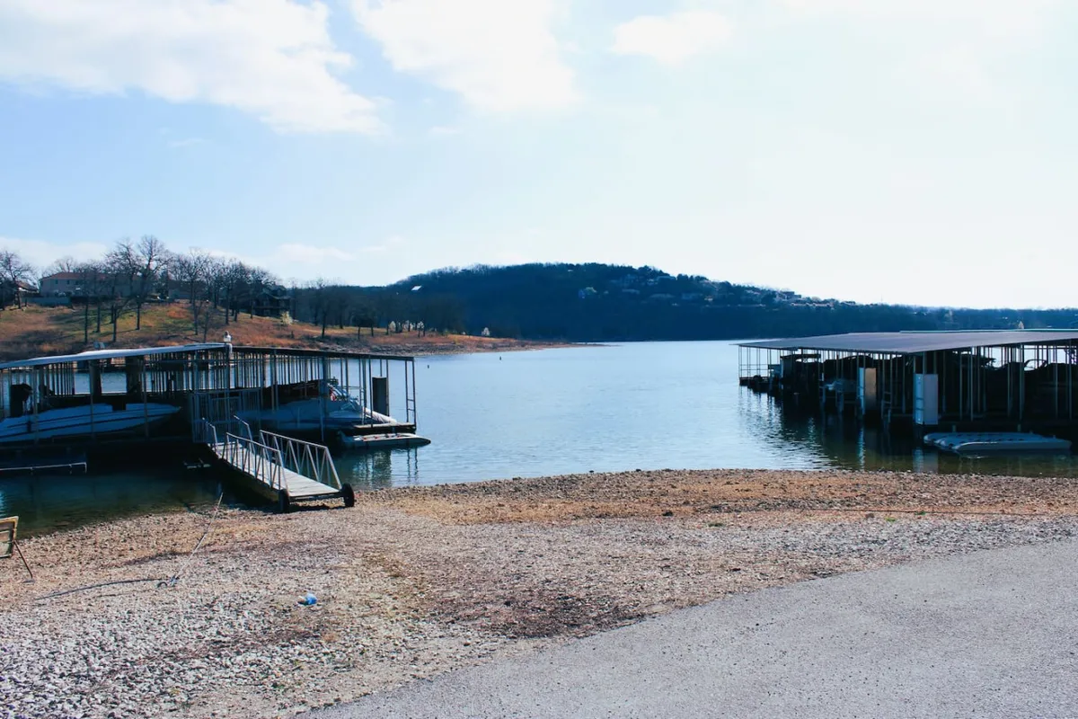 A serene view of boat docks on calm water, framed by rolling hills in the distance. The docks are ready for boats, and the setting sun casts a warm glow over the tranquil lake, capturing the peaceful atmosphere of dockside living.