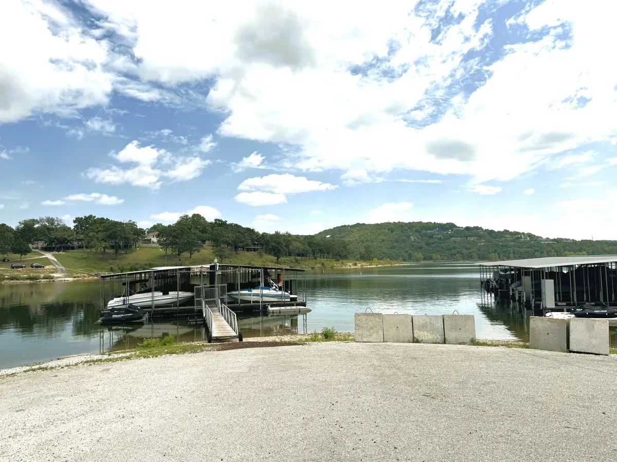 A tranquil lakeside view with boathouses on the water, calm reflections, and tree-covered hills in the distance, suggesting peaceful moments by the lake and easy access for boating or fishing.