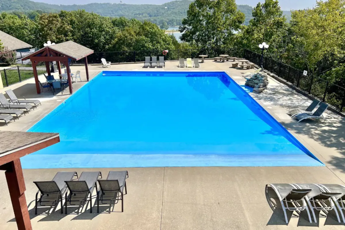 An inviting community swimming pool is surrounded by loungers, a gazebo, and lush greenery. The space feels welcoming and ideal for families to swim, relax, or enjoy a sunny afternoon together.