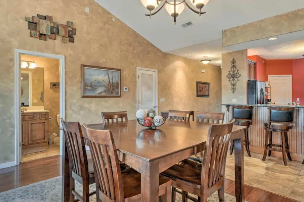 A welcoming dining area with a prominent table beneath an elegant chandelier, wall art for character, and an open kitchen visible in the background. The space is styled for both intimate family meals and larger group celebrations, capturing the essence of vacation gatherings and moments of connection.