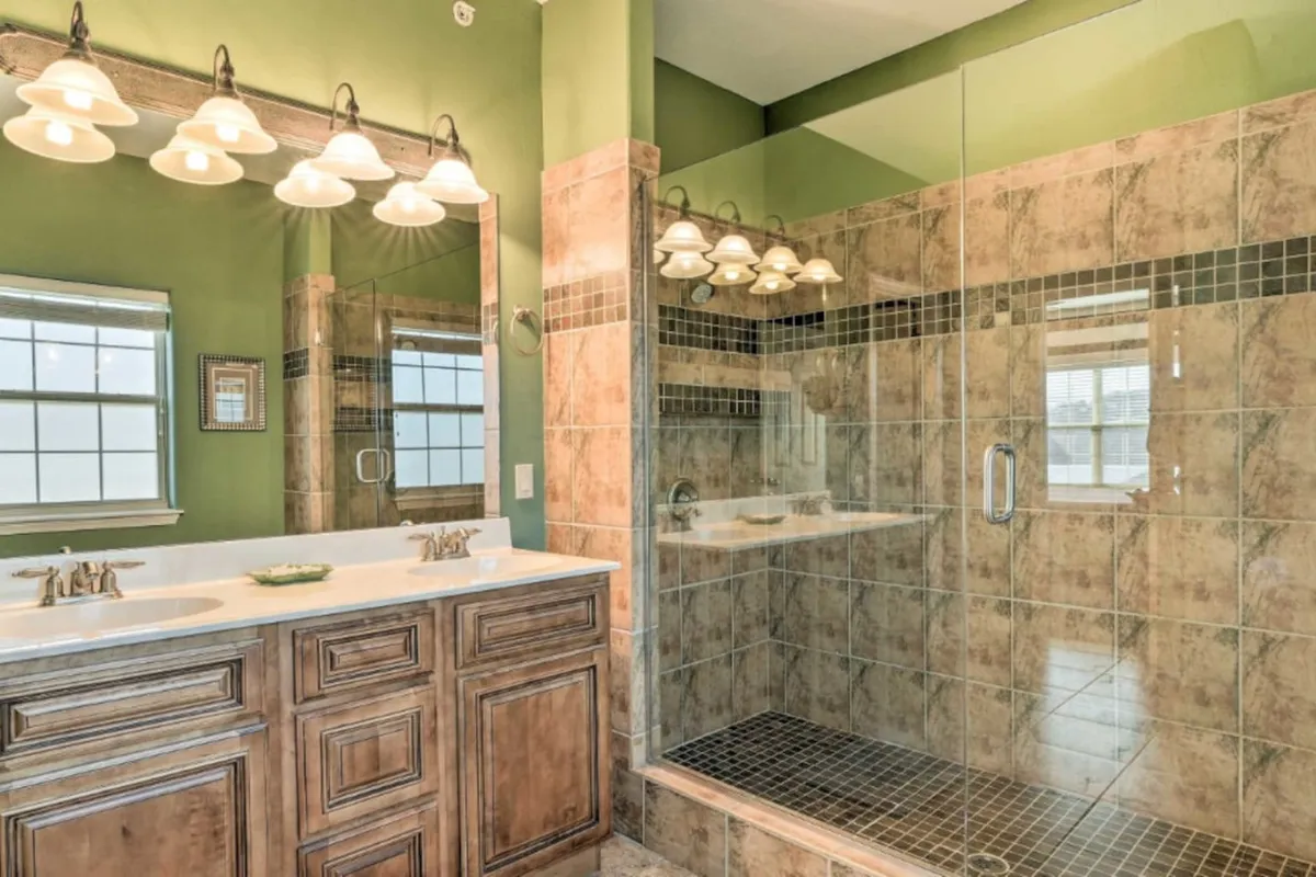 A luxurious, spa-like master bathroom featuring a glass shower enclosure, double sink vanity, elegant light fixtures, and a mirrored wall. The ambiance is both soothing and upscale, inviting relaxation and pampering.