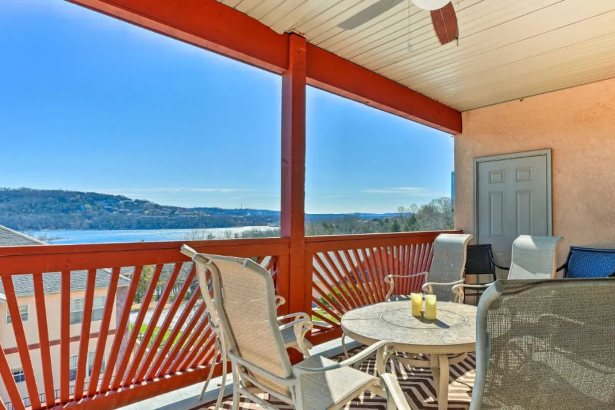 An inviting outdoor seating area rests atop a deck with expansive views over a serene lake. Candles on the table create a cozy, intimate atmosphere, and the surrounding treetops provide a lush natural frame. The image suggests tranquil moments spent relaxing and soaking in the breathtaking landscape, particularly at sunset.